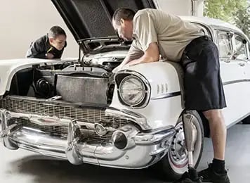man with prosthetic leg working on classic car with his son